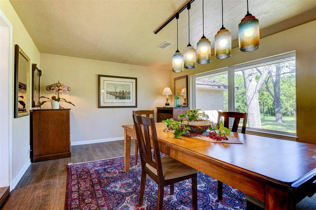 The picture windows frames a peaceful backyard view. The room blends charm with warm wood tones anchored by a statemnt chandelier.