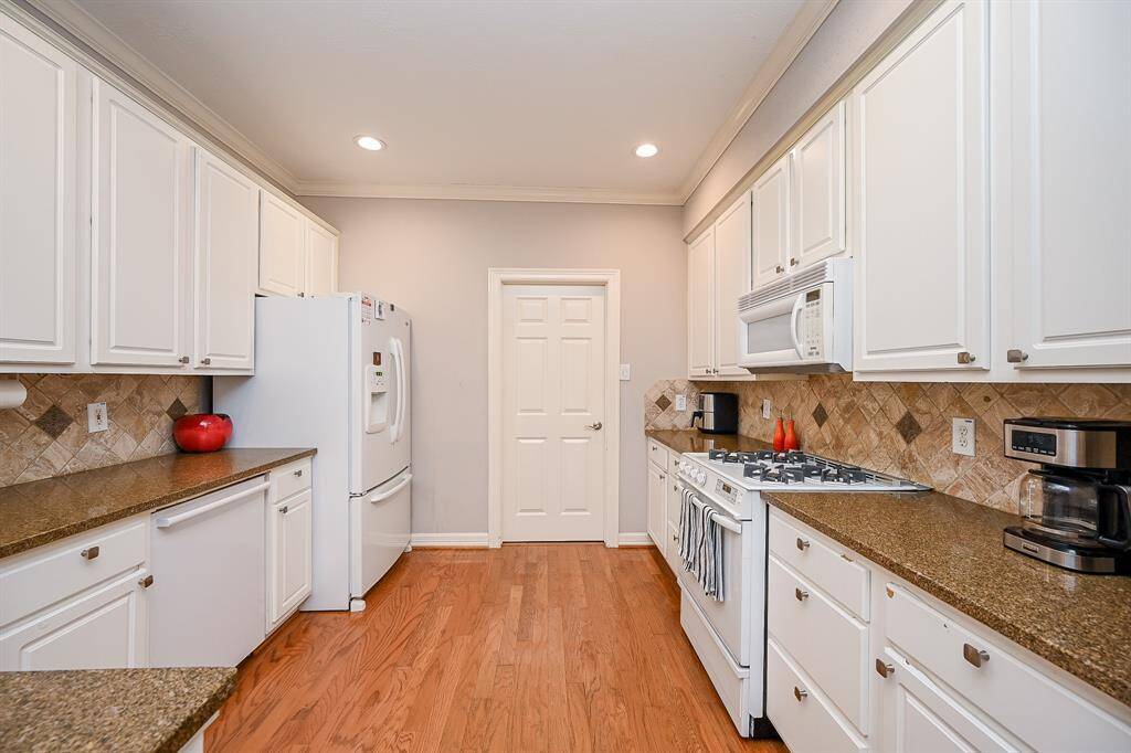 Every inch of wall and floor space in this spacious chef's kitchen is utilized with tons of white cabinetry, up and down, and contrasting caramel colored granite counters/mosaic-like tile backsplash. and amber colored flooring.