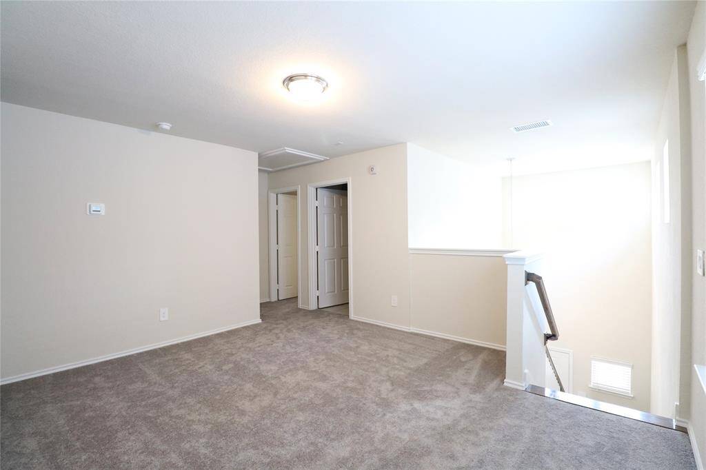 This photo shows a bright, carpeted upstairs landing area with neutral walls. It features a staircase with a railing, doors leading to other rooms, and ample natural light from large windows.
