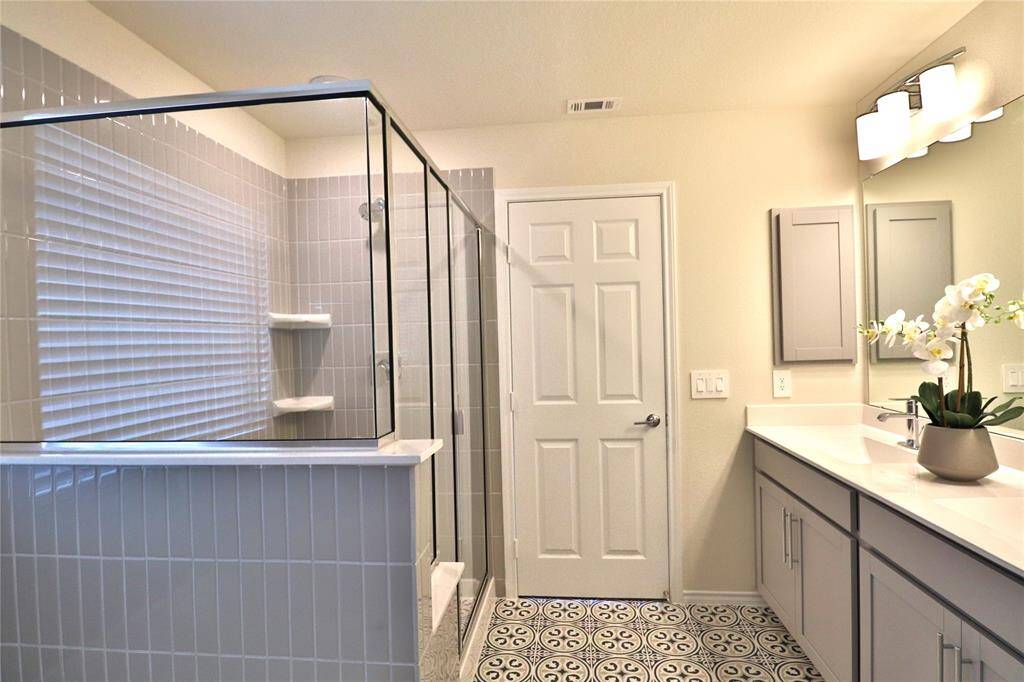 This bathroom features a spacious glass-enclosed shower, modern vanity with ample storage, elegant lighting, and decorative floor tiles, creating a sleek and stylish space.