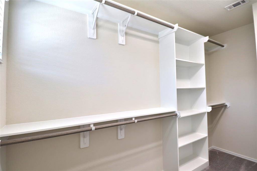 Spacious walk-in closet with multiple shelves and hanging rods for ample storage. Bright and well-organized, perfect for keeping clothes and accessories neatly arranged.