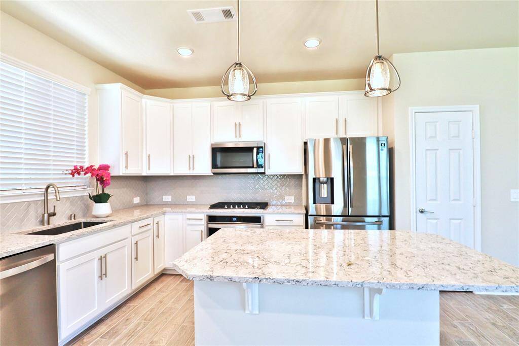 This kitchen features modern stainless steel appliances, white cabinetry, and sleek quartz countertops. It includes a center island with pendant lighting and a stylish tile backsplash, creating a bright and inviting cooking space.