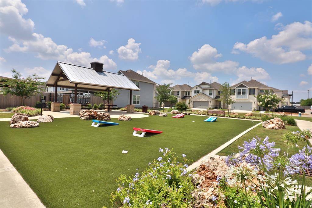 Charming neighborhood scene featuring a well-maintained communal green space with a covered picnic area, seating, and lawn games. it's perfect for family gatherings and outdoor activities