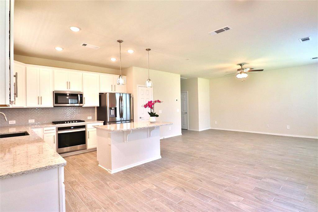 open-concept kitchen and living area. The living area has ample natural light and a ceiling fan, complemented by light wood flooring throughout.