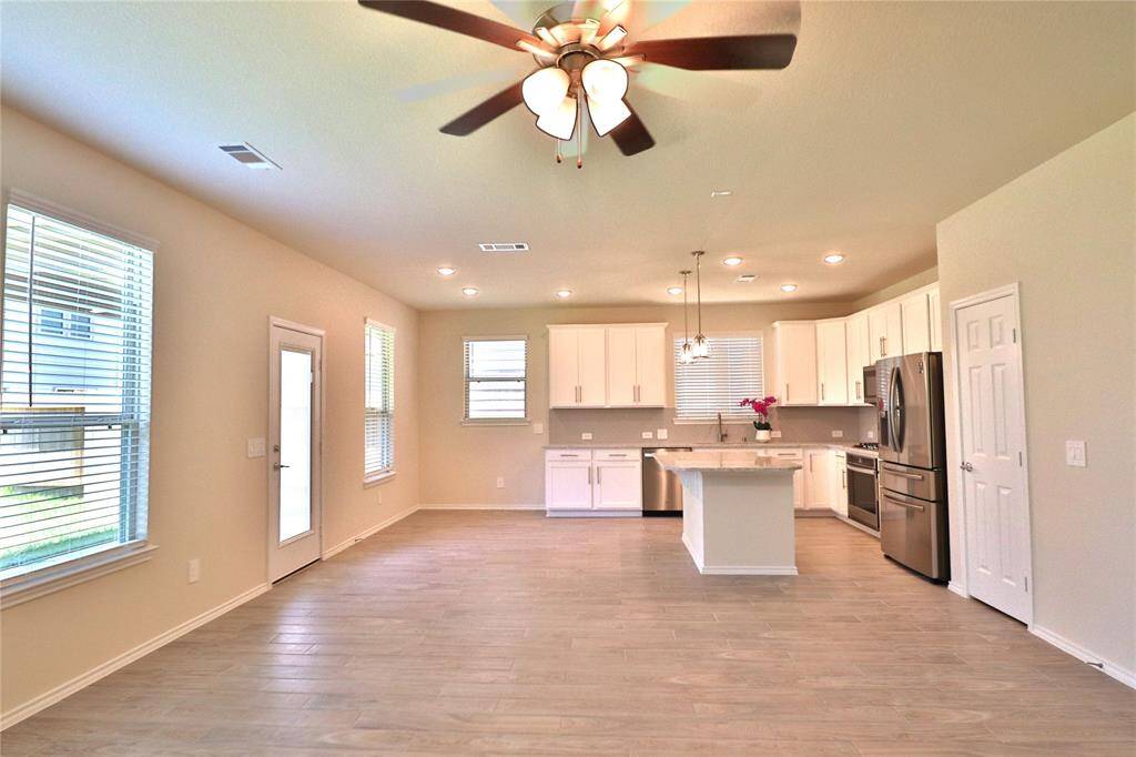 The area is enhanced by ample natural light from large windows and a glass door leading to the backyard, with elegant wood flooring and a ceiling fan .