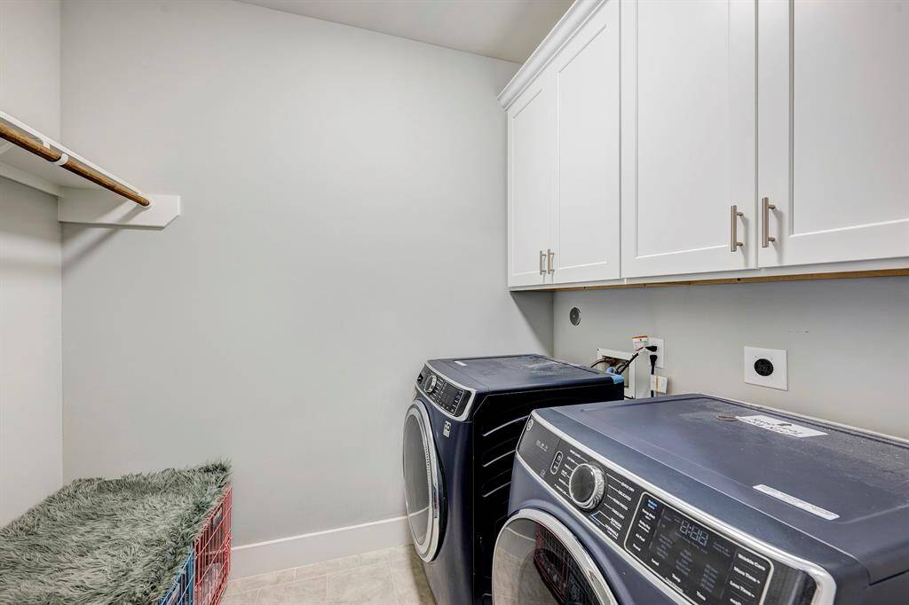 Utility room has tiled floor, space for full size washer & dryer, a hanging bar and storage cabinets.