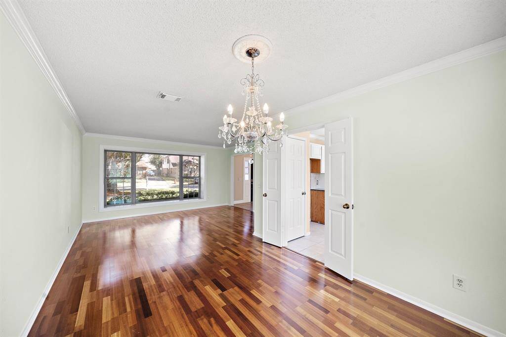 This spacious room features elegant hardwood flooring, a large window providing plenty of natural light, and a stylish chandelier. The neutral walls offer a blank canvas, and double doors lead to an adjacent space, adding versatility to the layout.