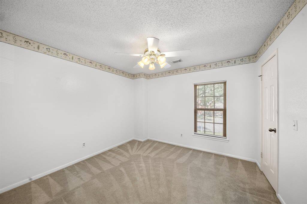 This room features neutral walls with a decorative border, carpeted floors, a ceiling fan with lights, and a window providing natural light. Ideal for a bedroom or home office.