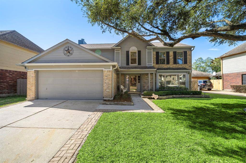 This charming two-story home features a spacious front yard with lush green grass, a well-maintained facade with a mix of stone and siding, and a two-car garage. The large windows and mature tree add character and provide ample natural light.