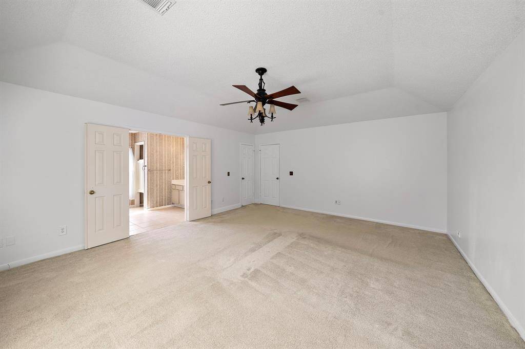 Spacious primary bedroom with neutral carpet, a large window for natural light, and a ceiling fan. Features double doors leading to your spacious bathroom