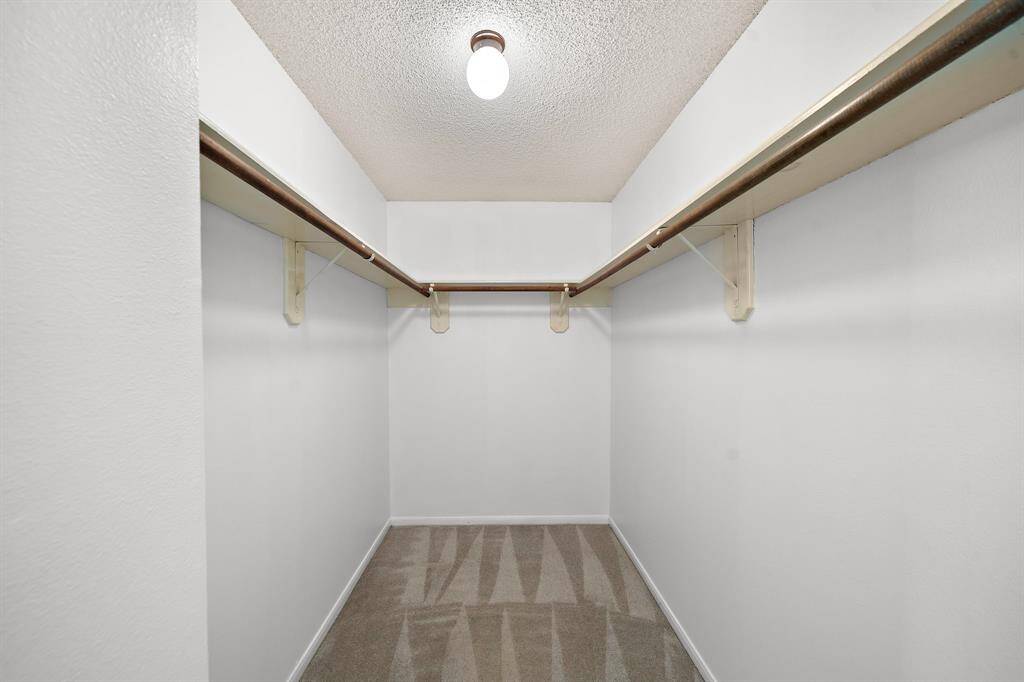 This is a spacious walk-in closet with clean white walls, a single light fixture, and ample hanging space on both sides, perfect for organizing clothes and accessories.