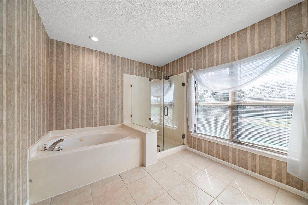 This primary bathroom suite features a spacious corner bathtub with  large windows offering natural light perfect soaking & relaxing.