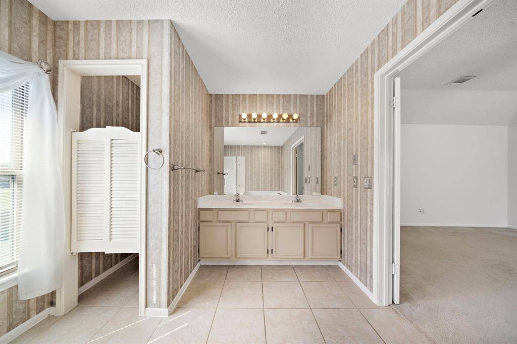This photo showcases a spacious bathroom with a double sink vanity, & large mirror.