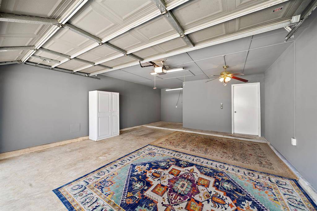 This spacious garage features a clean, gray interior with ample lighting, ceiling fans, and white storage cabinet provides additional organization.