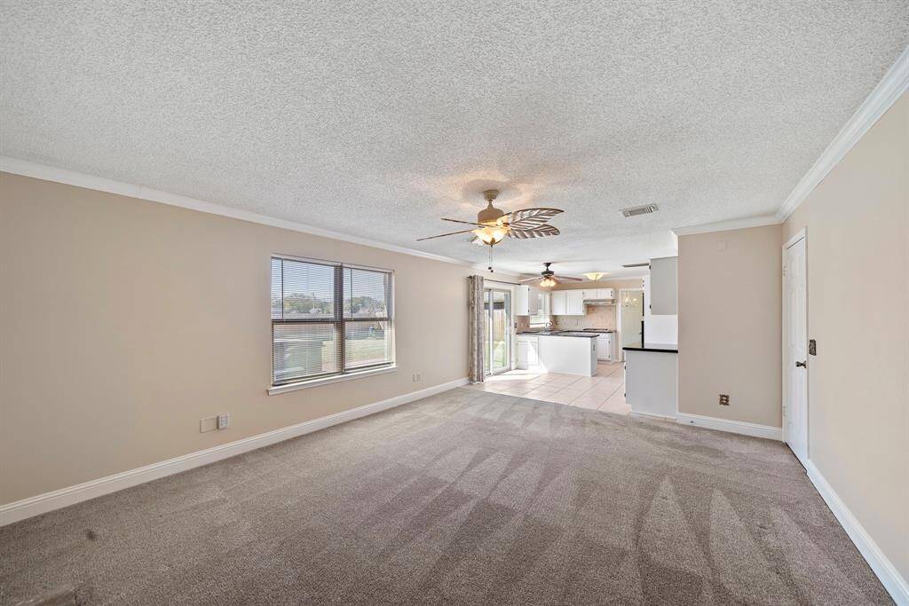 This photo showcases a spacious open-concept living and kitchen area with neutral walls. The kitchen features white cabinetry and a view of the backyard through sliding glass doors. Natural light fills the space, creating an inviting atmosphere.