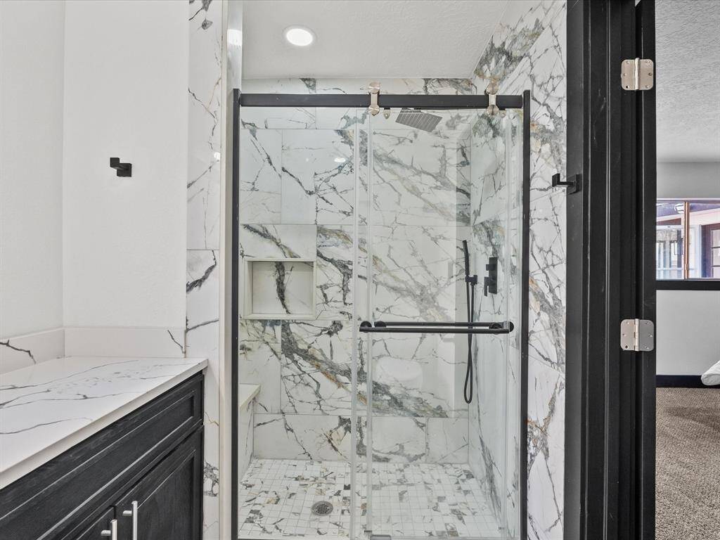 Modern bathroom featuring a glass-enclosed shower with elegant marble -like tiles and a sleek black-framed door.