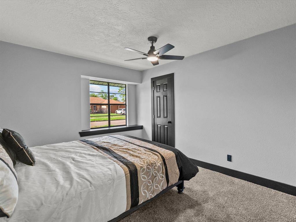 This photo showcases a cozy bedroom with neutral walls, a ceiling fan, and a large window providing natural light. The room is carpeted creating a welcoming atmosphere.