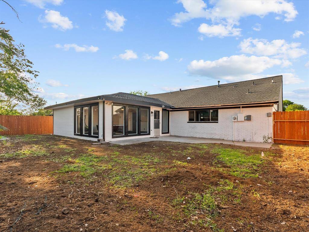 This photo showcases the backyard of a modern single-story home. It features a spacious patio area with large glass doors leading into the house, surrounded by a newly installed wooden fence.