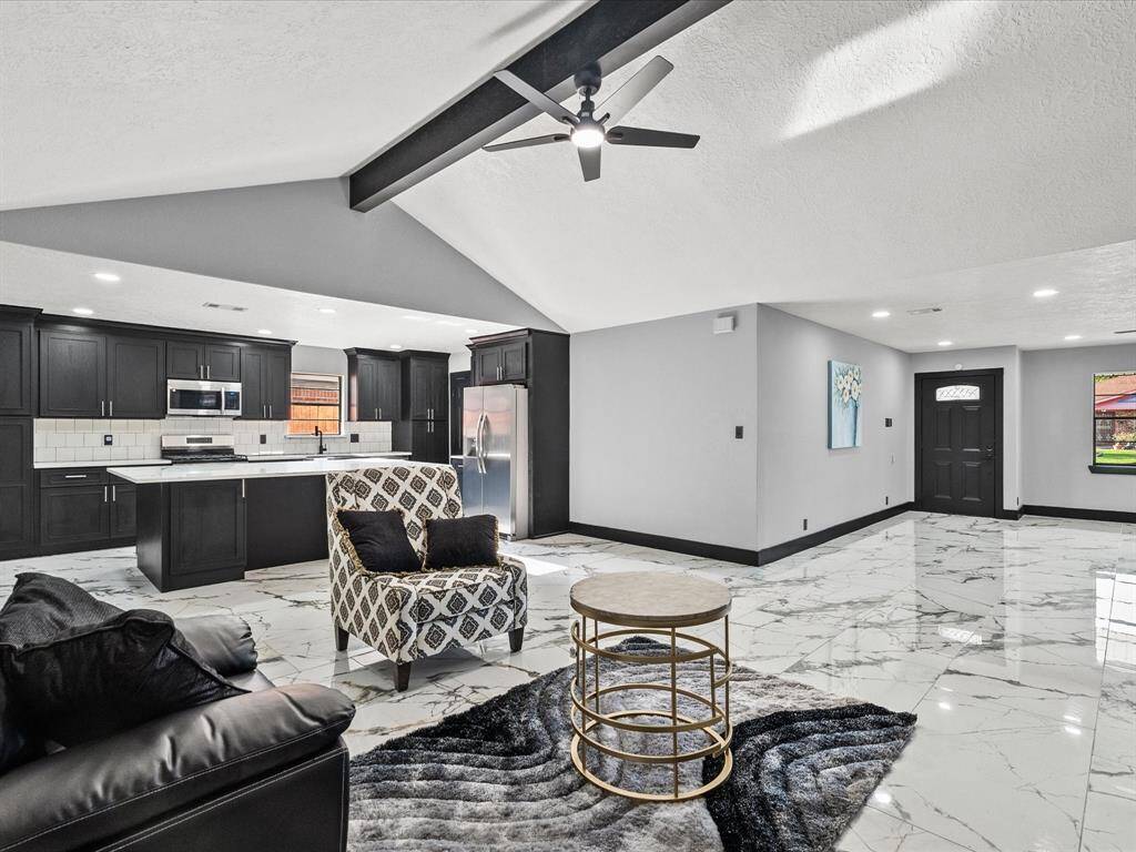 Spacious open-concept living area with elegant porcelain flooring and modern finishes. The kitchen features sleek black cabinetry, stainless steel appliances, and a central island. High ceilings and a ceiling fan enhance the airy feel, while contemporary decor adds a touch of sophistication.