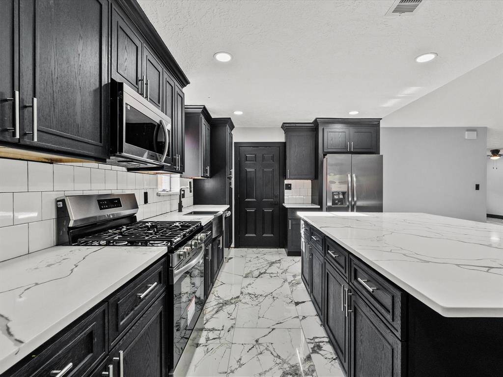 The kitchen space is brightened by white tile backsplash and recessed lighting, creating a sophisticated and functional cooking area.