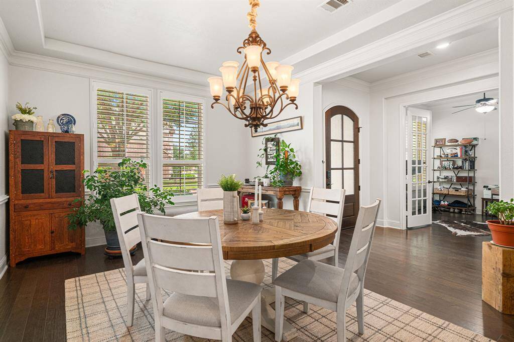 Gorgeous formal dining room with tray ceiling, crown molding, chair rail, elegant chandelier, plantation shutters, and hardwood floors.