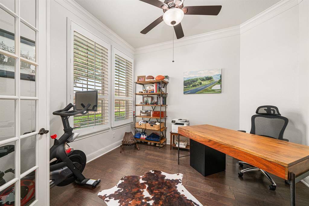Private office at the front of the home behind glass French doors features hardwood floors, crown molding, and plantation shutters.
