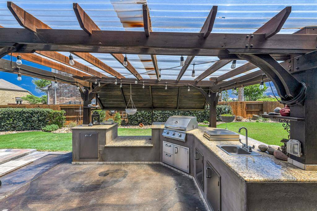 This outdoor kitchen features granite countertops, a natural gas grill, a custom counter spot for a Big Green Egg Grill, electric outlets, and a sink.