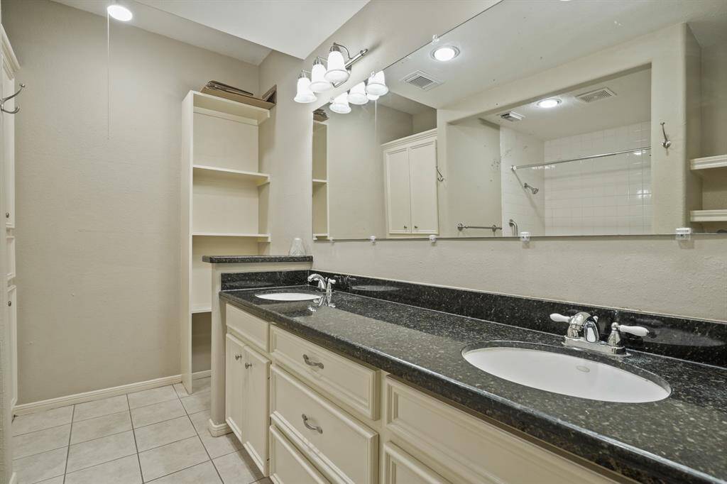 The primary en-suite bathroom features tile floors, dual sinks, dark countertops, and plenty of storage space.