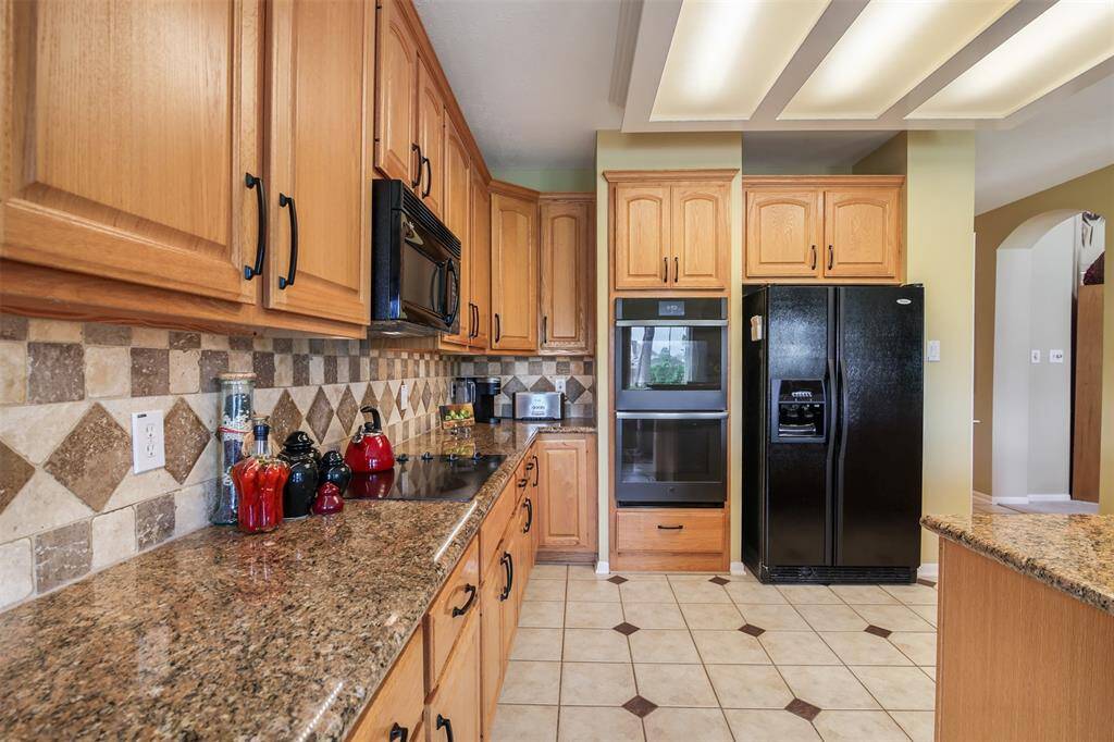 Another view of the kitchen with tile backsplash, matching black appliances and double ovens. Ovens replaced in 2022.