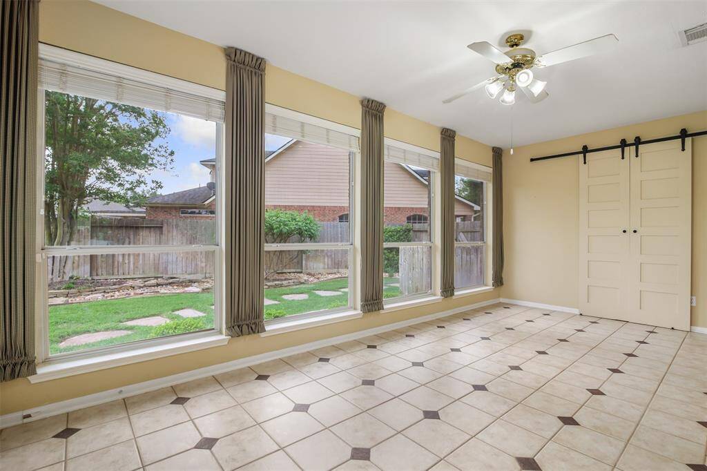 Huge sunroom with wall of windows, tile flooring and sliding barn doors leading to a large storage closet. This would have originally been the third bay of a tandem garage.