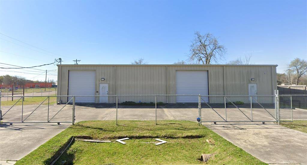 This property features a large metal building with two roll-up garage doors and a side entry door, surrounded by a secure chain-link fence. It's suitable for storage or workshop purposes.