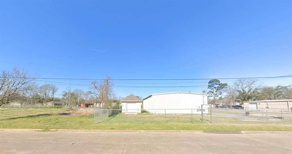This property features a spacious lot with a fenced area, a small white structure, and a large adjacent building. It's a flat, open space suitable for various uses, offering potential for development or storage.