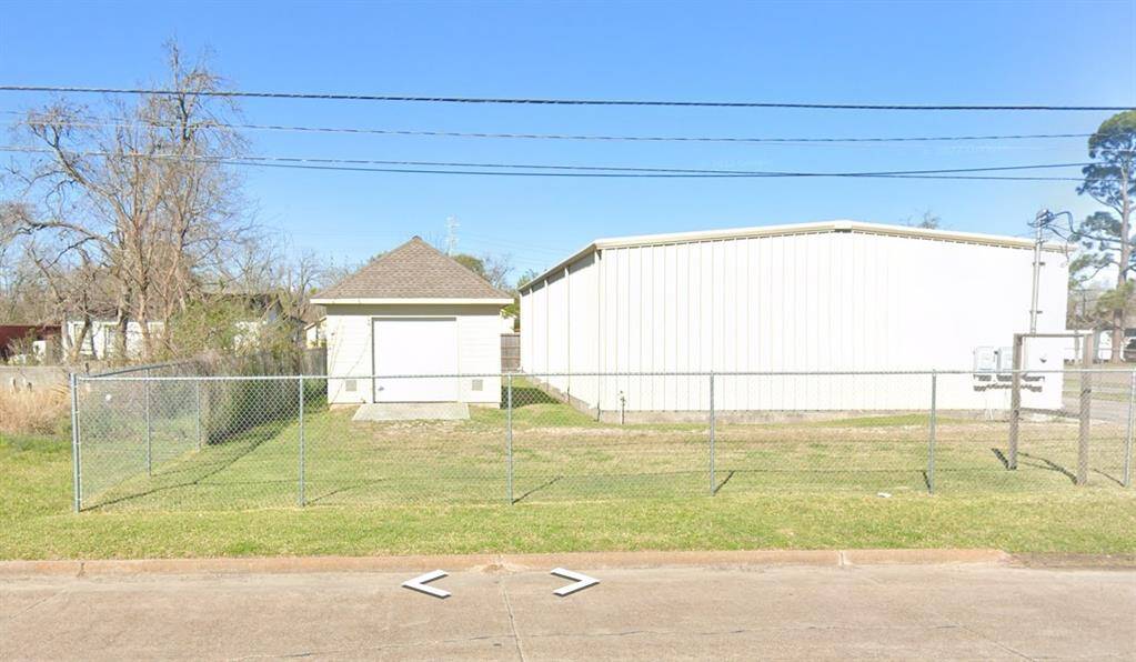 Spacious fenced lot featuring a small shed and a large metal building, ideal for storage or workshop purposes. Ample open space and easy access from the street.