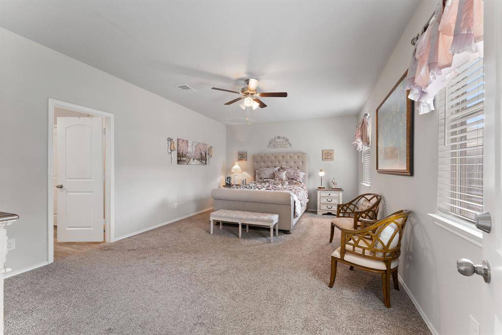 This over-sized primary bedroom boasts with neutral paint tones, a ceiling fan for added comfort, and plush carpeting