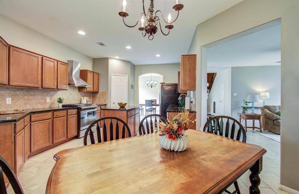 This photo showcases a spacious kitchen and dining area with warm wooden cabinetry, modern stainless steel appliances, and a cozy dining table. The open layout allows for easy flow into a well-lit living room, creating an inviting space perfect for family gatherings and entertaining.