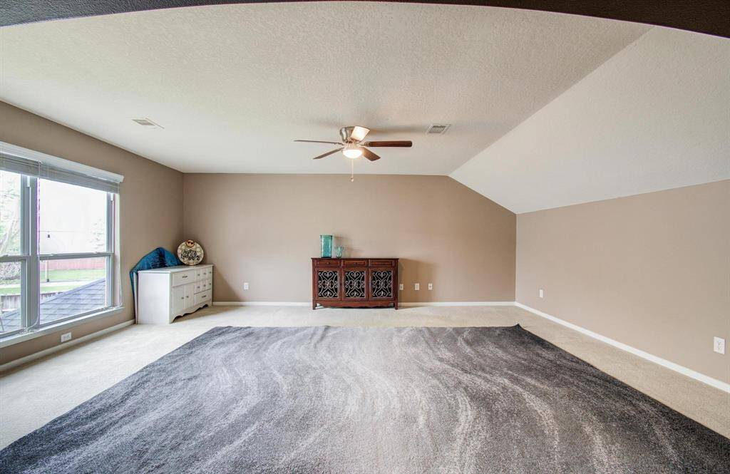 This spacious room features a neutral color scheme, large windows offering plenty of natural light, and a ceiling fan for comfort. It's perfect for a variety of uses, with ample wall space and a cozy carpeted area.