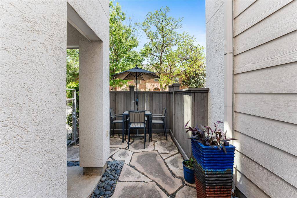 Cozy outdoor patio area with stone flooring and a modern blue planters with greenery. It's enclosed by a wooden fence, providing privacy and a serene space for relaxation.