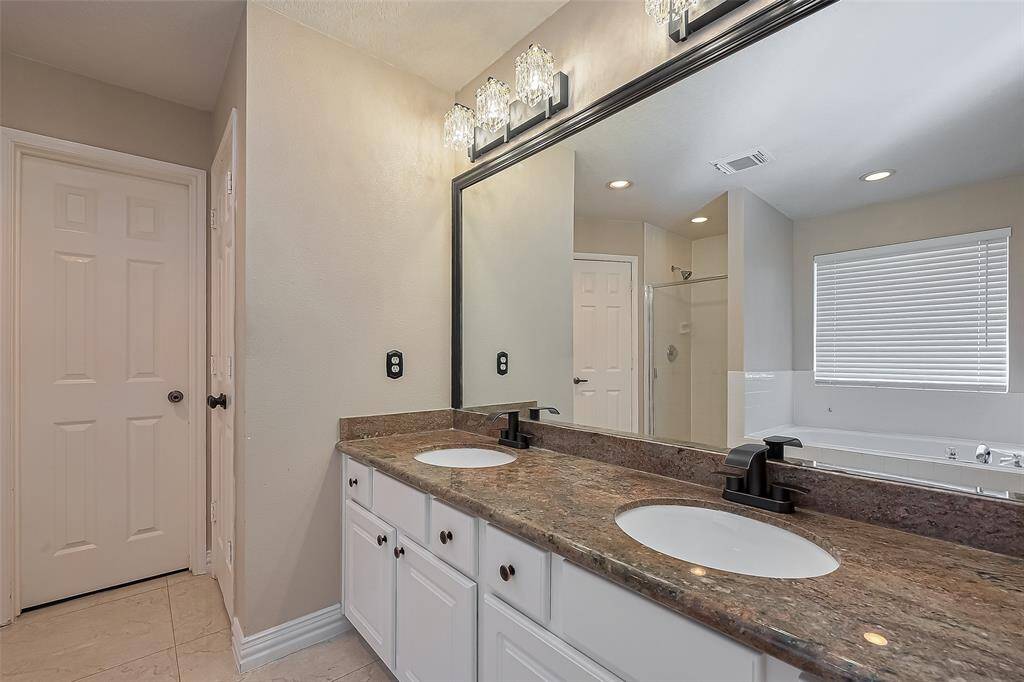 Primary bathroom features a double vanity with elegant granite countertops and modern fixtures. It includes a large mirror with stylish lighting, a shower, and a separate bathtub, complemented by neutral-toned walls and floor tiles.