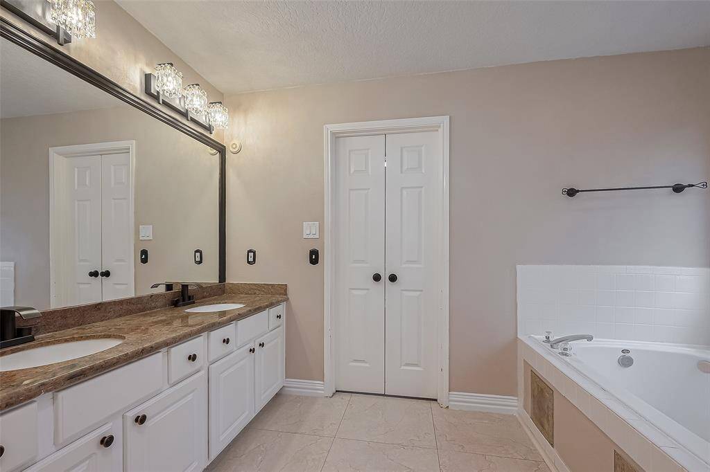 Luxurious primary bathroom featuring dual sinks, elegant lighting, and a relaxing soaking tub.