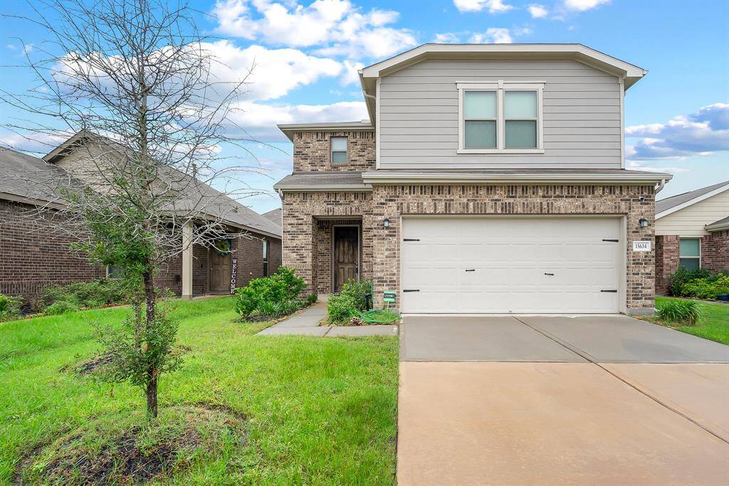 Welcoming two-story home with charming brick facade, spacious driveway, and lush front fall lawn.