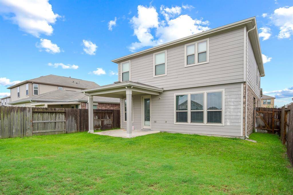 The backyard of a two-story home with a covered patio and fenced yard, ideal for outdoor activities. The exterior features light toned siding and multiple windows, offering a spacious and private setting.