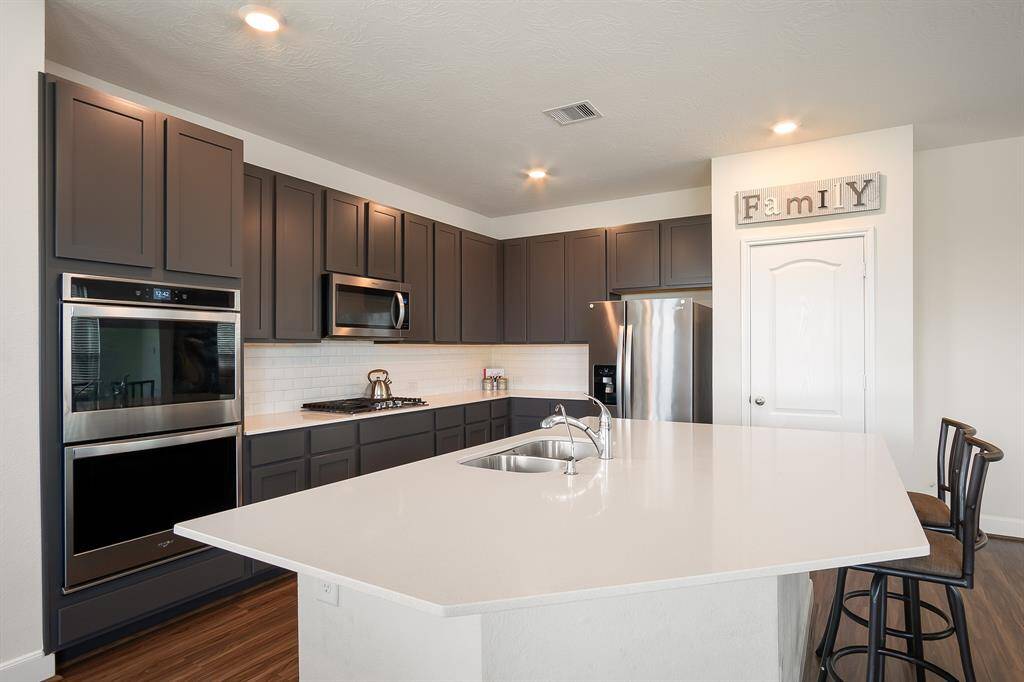 This modern kitchen features sleek dark cabinetry, stainless steel appliances, and a spacious white island with a built-in sink.