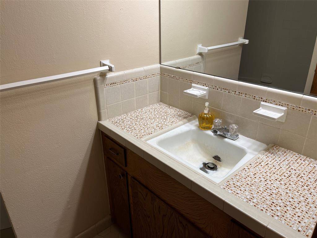 The first room on the left side of the hallway is the guest bath. It features vintage tile and the sink was accidentally damaged with some chemicals that were not designed for a porcelain finish. You can see the tub/shower reflected in the mirror.