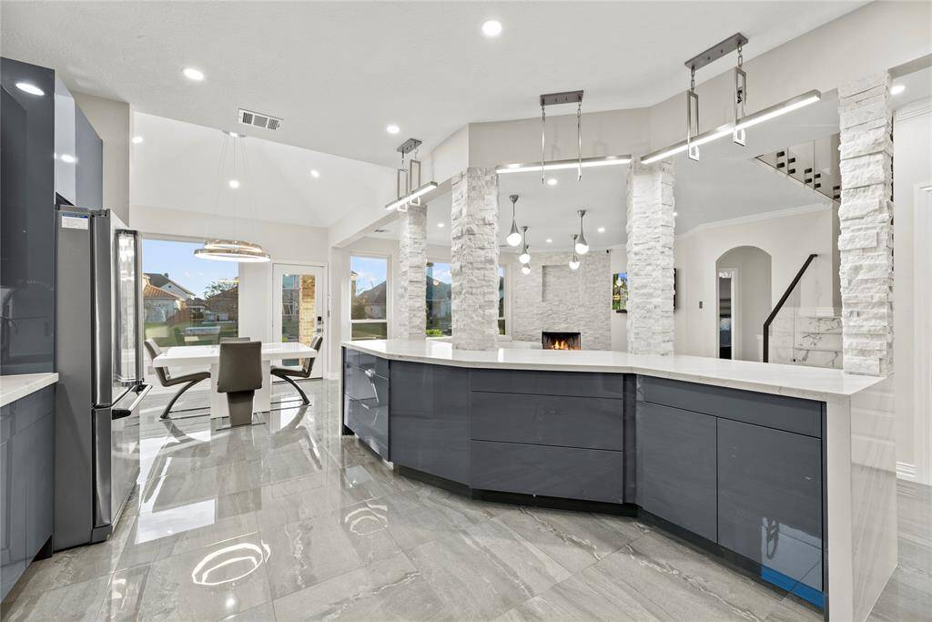 Open-concept kitchen with a curved island, modern pendant lighting, tile floors, and a seamless flow into the family room—perfect for culinary enthusiasts and entertaining.