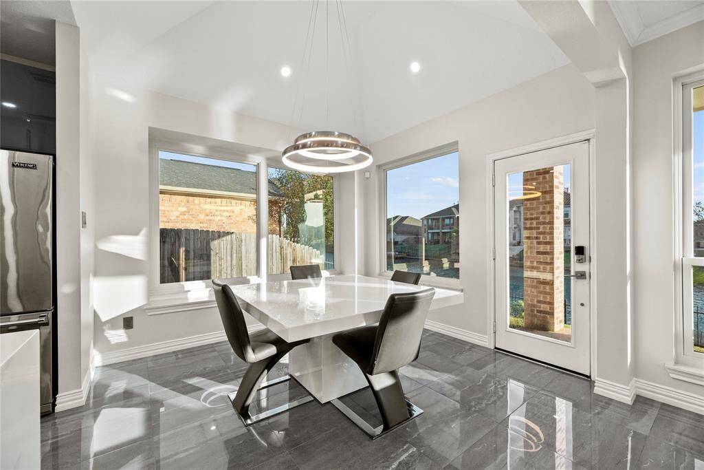 Bright and modern breakfast room featuring large windows with tranquil views, tile floors, and a stylish contemporary chandelier—perfect for enjoying morning coffee or intimate meals.
