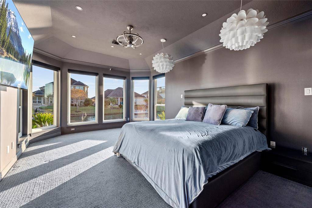 Spacious primary bedroom with panoramic water views, modern lighting fixtures, and a serene ambiance, creating a retreat for relaxation and comfort.