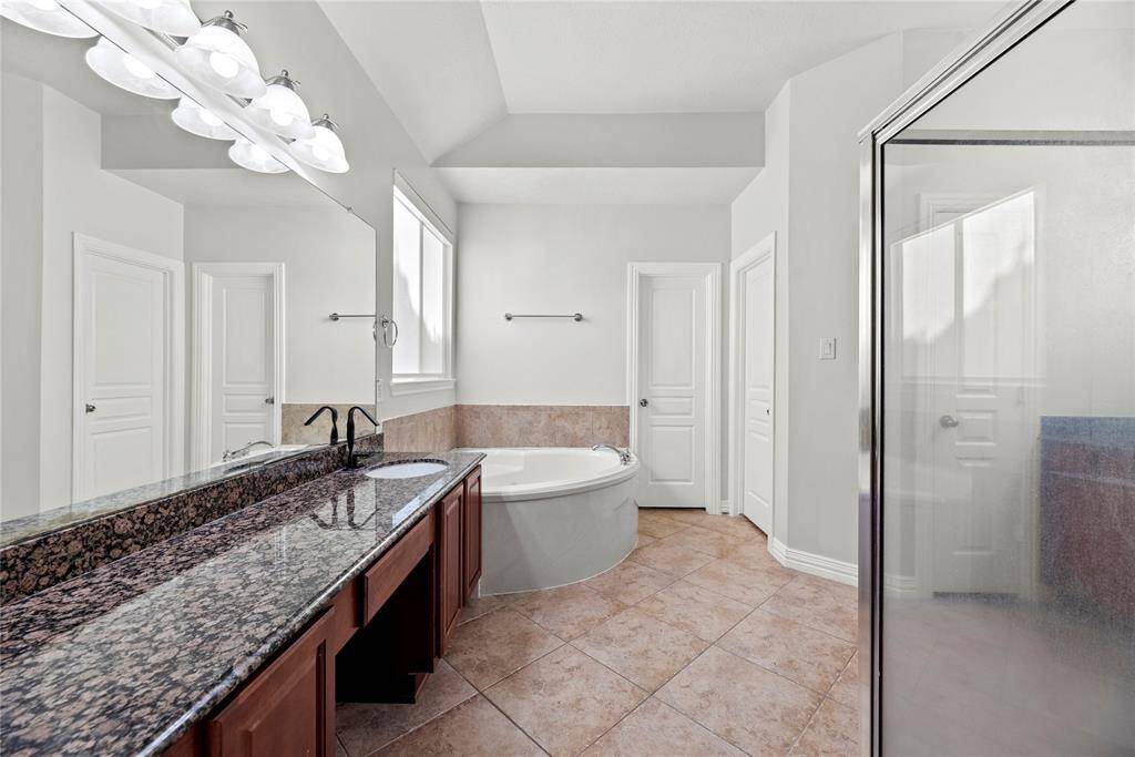 Luxurious primary bathroom featuring dual vanities with granite countertops, a relaxing jetted tub, a separate glass-enclosed shower, and ample natural light for a spa-like experience.