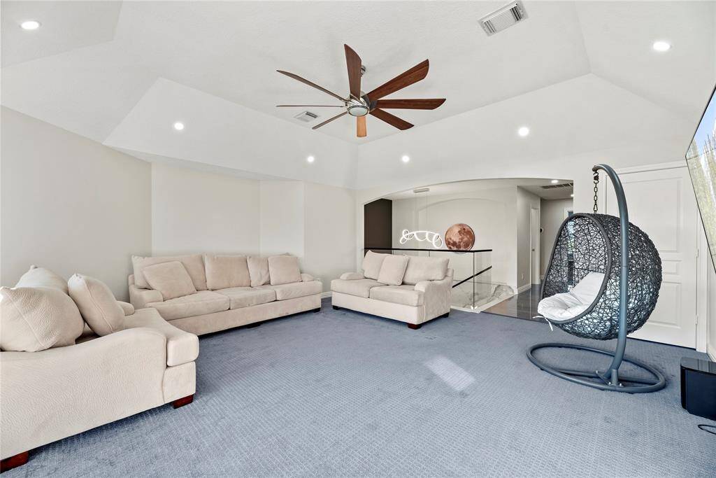 Expansive upstairs game room featuring plush carpeting, a modern ceiling fan, and plenty of room for lounging or entertaining, with stylish design elements and natural light throughout.