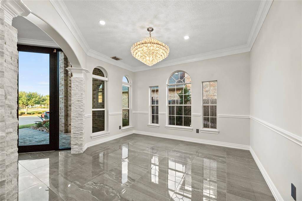 Bright and elegant formal living room featuring a sparkling chandelier, arched windows for abundant natural light, and polished floors reflecting timeless sophistication.