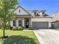 Charming single-story house with a stone and brick exterior and a neatly landscaped front yard. It features a spacious driveway leading to a two-car garage, and an inviting front porch.
